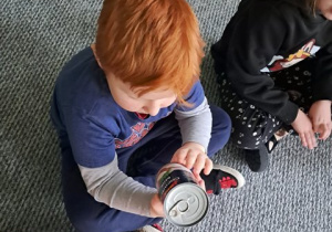 Chłopiec siedzi na dywanie i ogląda puszkę mleka kokosowego