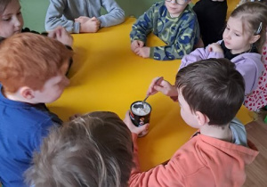 Dzieci podczas warsztatów siedzą przy stoliku i obserwują chłopca, który miesza mleko kokosowe