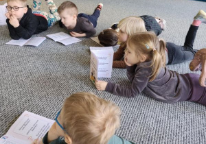 Dzieci leżą na dywanie i oglądają książeczki