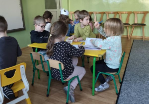 Dzieci siedzą przy stolikach i wykonują rysunki w swoich książeczkach