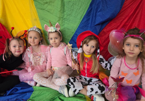 Dziewczynki w strojach karnawałowych siedzą na kolorowej chuście