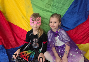 Dziewczynki w strojach karnawałowych siedzą na kolorowej chuście