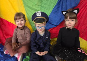 Dzieci w strojach karnawałowych siedzą na kolorowej chuście