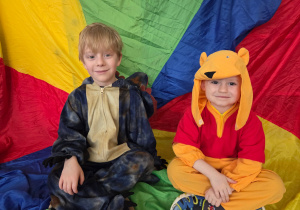 Chłopcy w strojach karnawałowych siedzą na kolorowej chuście