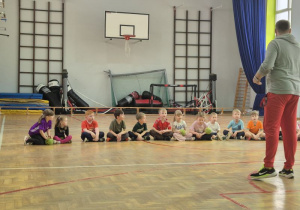 Dzieci siedzą skrzyżnie obok siebie i trzymają piłki w dłoniach