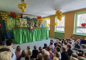Dzieci siedzą na widowni, oglądają teatrzyk, na scenie słonik pacynka i wiewiórka