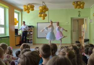 Dzieci oglądają występ - taniec baletnic ubranych w białe stroje z niebieską i różową spódnicą
