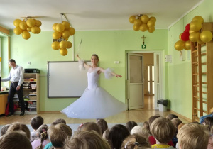 Dzieci oglądają występ - taniec wróżki ubranej w białą suknię i trzymającą różdżkę w dłoni