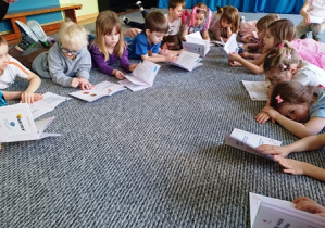 Dzieci leża na dywanie i przeglądają strony książek