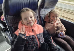 Dwie dziewczynki siedzą w autokarze i machają ręką