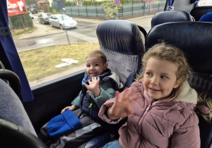 Chłopiec z dziewczynką siedzą w autokarze i machają do zdjęcia