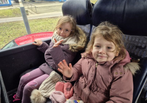 Dwie dziewczynki siedzą w autokarze i machają ręką