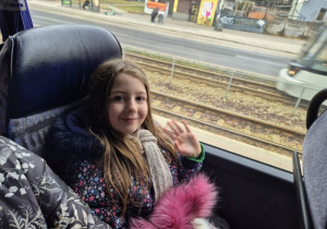 Dziewczynka siedzi w autokarze i macha ręką