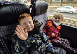 Chłopiec z dziewczynką siedzą w autokarze i machają ręką