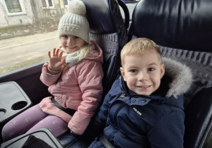 Chłopiec z dziewczynką siedzą w autokarze i machają ręką