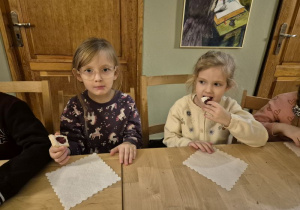 Dziewczynki siedzą przy stoliku i jedzą ciasteczka