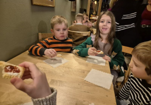 Dzieci siedzą przy stoliku i jedzą ciasteczka