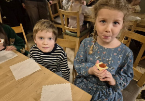 Dzieci siedzą przy stoliku i jedzą ciasteczka