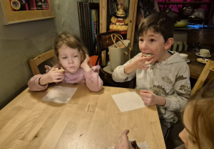 Dzieci siedzą przy stoliku i jedzą ciasteczka