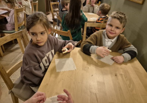 Dzieci siedzą przy stoliku i jedzą ciasteczka