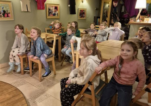 Dzieci siedzą na krzesełkach i czekają na rozpoczęcie przedstawienia