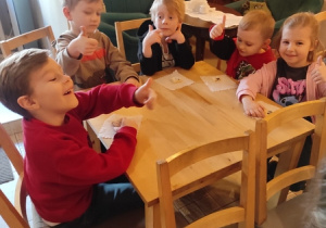 Dzieci przy stolikach jedzą ciastka.