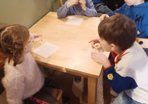 Dzieci siedzą przy stoliku i jedzą ciasteczka