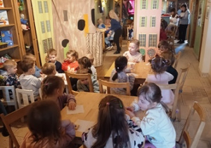 Dzieci siedzą przy stolikach w oczekiwaniu na poczęstunek