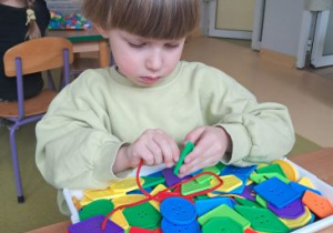 Chłopiec przekłada sznurek przez dziurki guzików