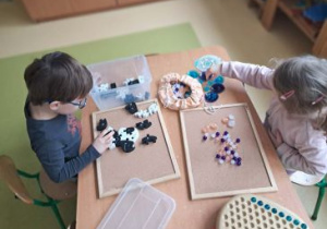 Dzieci siedzą przy stoliku i pracują na materiale rozwojowym