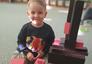 Chłopiec prezentuje swoją konstrukcję z różowej wieży i brązowych schodów