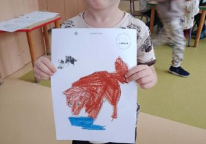 Chłopiec prezentuje kolorowankę przedstawiajacą psa