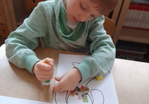 Chłopiec wykleja kolorowymi kawałkami gazety sylwetę psa