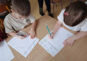 Dzieci siedzą przy stoliku i rysują po śladzie