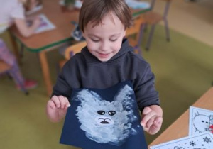 Chłopiec pozuje do zdjęcia trzymając w ręku swoją pracę plastyczną