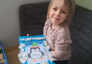 Dziewczynka prezentuje swoją pracę przedstawiającą pingwina