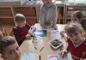Dzieci siedzą przy stoliku i kolorują misie