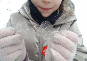 Dziewczynka pozuje do zdjęcia i trzyma w dłoniach kawałki lodu