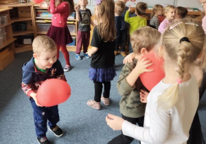 Dzieci podczas zabawy tanecznej z czerwonymi balonami w kształcie serduszek