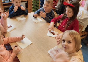 Dzieci siedzą przy stolikach i jedzą walentynkową czekoladę