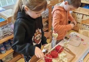 Dziewczynka wykonuje walentynkową pracę: układa serduszka na patyczkach w czerwonych wstążkach