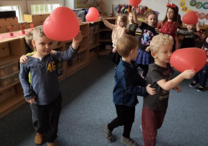 Dzieci podczas zabawy tanecznej z czerwonymi balonami w kształcie serduszek