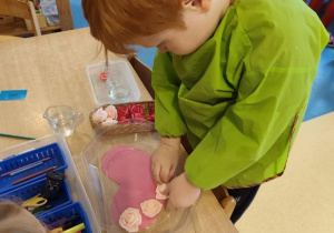 Chłopiec wykonuje walentynkową pracę: układa róże na serduszku zalanym wodą