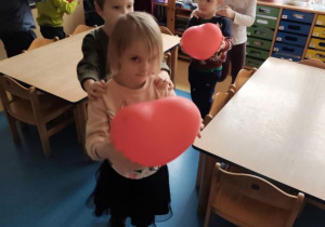 Dzieci jadą w pociągu jedno za drugim trzymając w dłoniach czerwone balony w kształcie serca