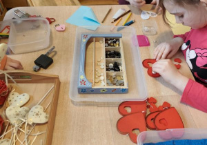 Dziewczynka wykonuje walentynkową pracę: przykleja kolorowe kamyczki do drewnianych serduszek