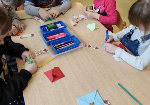 Dzieci siedzą przy stoliku i przygotowują kartki walentynkowe dla innych dzieci