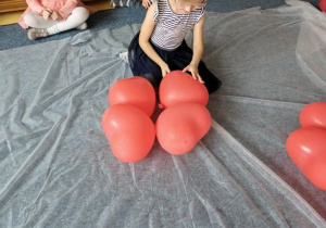 Dziewczynka wybiera balon spośród leżących na białym materiale