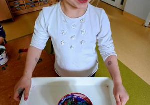 Dziewczynka trzyma w dłoniach tace z pomalowanym śniegiem