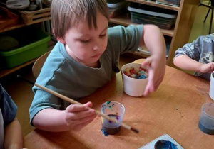 Tymon podczas zabawy badawczej nabiera farbę na pędzel