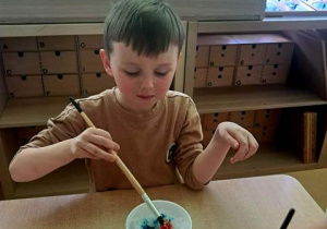 Chłopiec w czasie zabawy badawczej maluje śnieg farbami